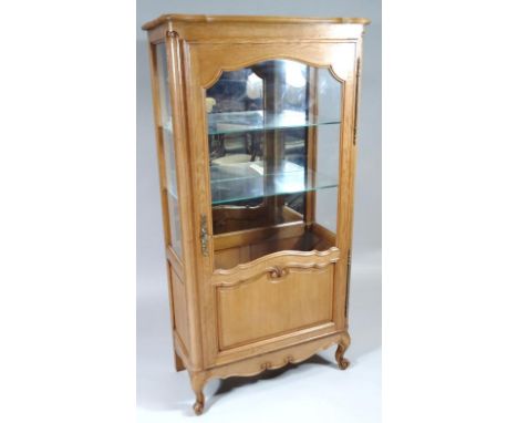 A 20thC light oak display cabinet, the shaped top raised above a single door revealing shelves,  with glazed sides, front and