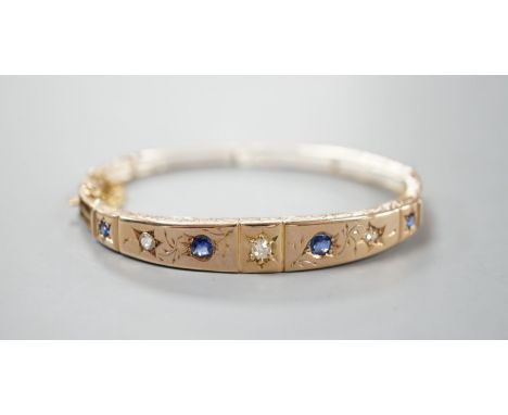 A late Victorian engraved yellow metal, four stone sapphire and three stone diamond set hinged bangle, gross 10.5 grams.