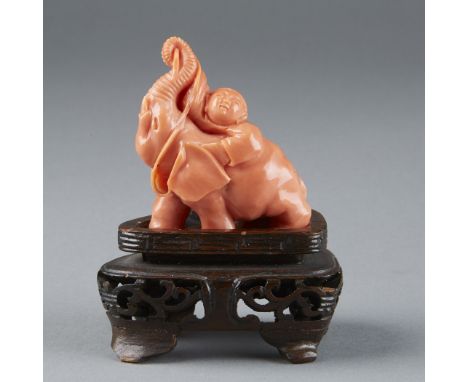 Beautiful coral figurine of a boy climbing onto an elephant.  The elephant appears to be helping the boy by pulling up his ba