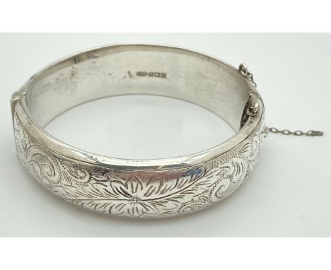 A vintage silver hinged bangle with half engraved detail. Safety chain broken. Hallmarked Birmingham 1964. Approx. 6cm diamet