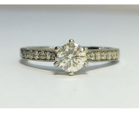 A Contemporary Solitaire Diamond Ring with Platinum Shank, with Diamond Set Shoulders. The ring has a central brilliant cut d
