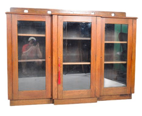 An late 19th Century Arts &amp; Crafts oak breakfront display cabinet / bookcase having a raised gallery back with carved hea