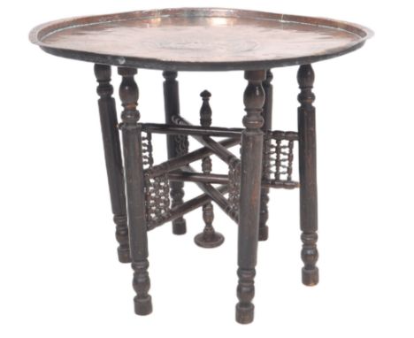 A 19th Century carved Benares table having a brass tray top engraved with leaves, objects and central medallion raised on fol