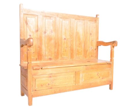 A large 20th Century Country Farmhouse pine settle bench having a tall panelled back rest with scrolled armrests and lift up 
