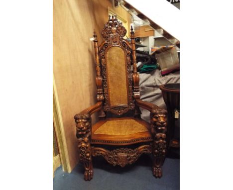 A large 20th C German carved mahogany throne style elbow chair, the back heavily carved with scrolling foliate, shields and c