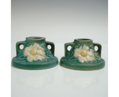 A pair of dainty pottery candle stick holders carefully decorated with irregular clusters of flowers set on a green textured 