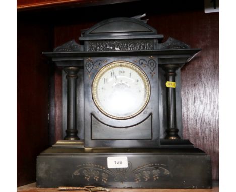 A black marble arch top mantel clock with engraved decoration, enamelled dial and Arabic numerals, flanked by metal fluted co