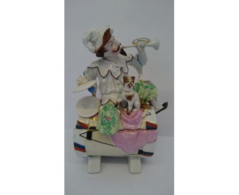 A Continental china jar and cover modelled as a Jester playing a trumpet and cymbals with a dog by his side, seated on a drum