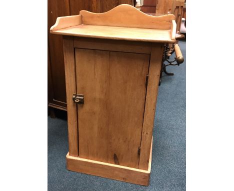 A pine bedside cabinet with shaped upper border above a grooved door enclosing a shelf on plinth base, with towel rail to one