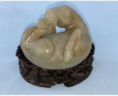 A Chinese jade coloured hardstone carving of a foal curled up on associated intricately carved wooden stand length 8.5cm, hei