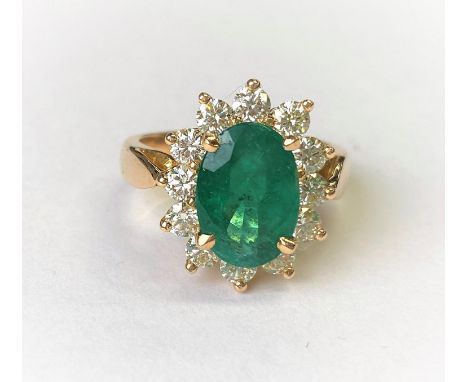 An 18ct gold dress ring set with a large faceted oval emerald, 11mm x 7mm and surrounded by 12 diamonds, 2.9mm approximate di