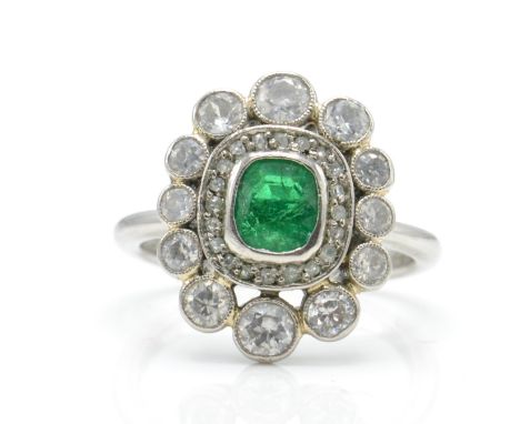 A hallmarked platinum emerald and diamond cluster ring. The ring set with a central emerald surrounded by graduating halos of