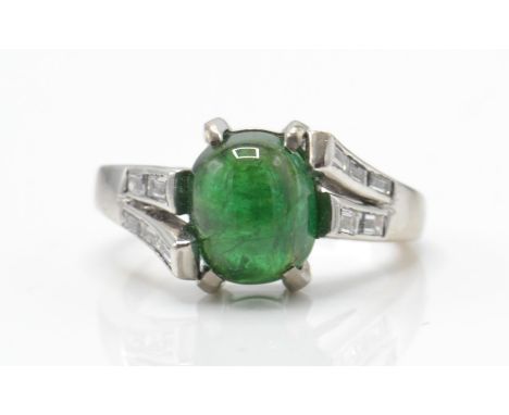 A 20ct white gold emerald and diamond ring. The ring set with an emerald cabochon within a prong setting having split diamond