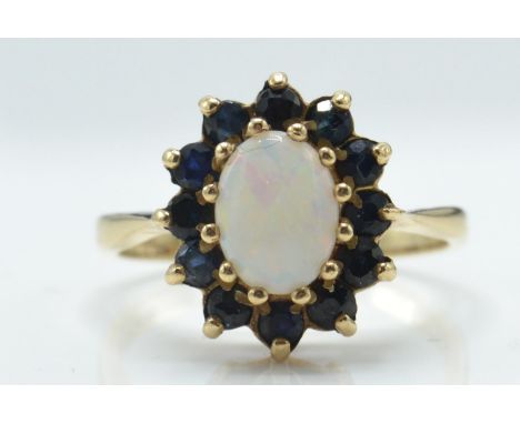 A 9ct gold opal and sapphire cluster ring. The London hallmarked ring with opal cabochon within a halo of sapphires with bask