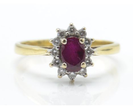 A hallmarked 18ct gold ruby and diamond cluster ring. The ring set with a central mixed cut oval ruby surrounded by a halo of