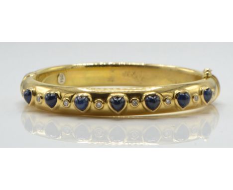 An 18ct gold sapphire and diamond bangle. The bangle set with heart shaped sapphire cabochons with diamond spacers having hid