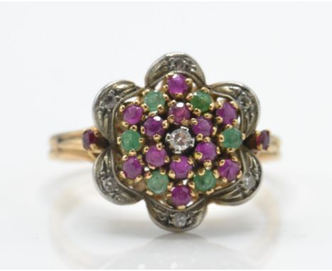 A gold ruby and diamond cluster ring. The ring set with a central single cut diamond surrounded by mixed cut rubies and emera