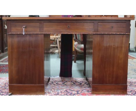 An early 20th century mahogany pedestal desk with central long drawer flanked by short drawers over cabinet doors on plinth b