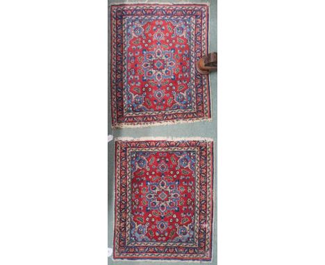 A pair of small red ground isfahan style rugs with light blue floral medallions, matching spandrels and flower head borders, 