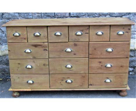 A stripped pine dresser fitted with an arrangement of fifteen drawers with vintage style cast metal cup handles, raised on tu