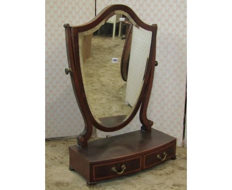 An Edwardian mahogany shield shaped toilet mirror with bevelled edge plate raised on a bow fronted box base with two frieze d