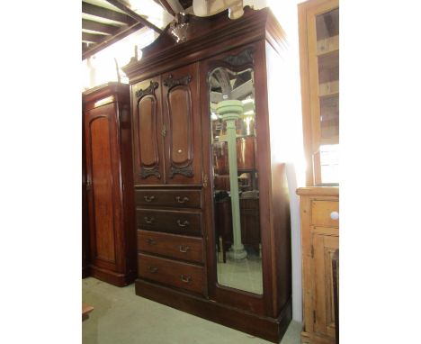 An Edwardian mahogany compactum wardrobe enclosed by three doors and four long drawers, mirror and fielded panelled with carv