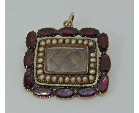 Antique yellow metal mourning brooch / pendant set with borders of flat cut garnets and seed pearls surrounding a central gla