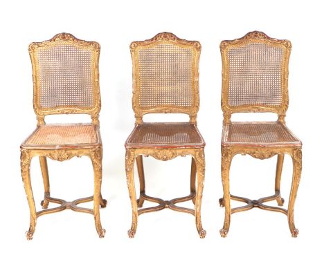 A set of three French Louis XVI style giltwood and gesso salon side chairs with caned seats and cabriole legs with shell and 