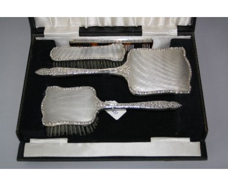 A CASED SILVER MOUNTED FOUR PIECE DRESSING TABLE SET, having engine turned decoration with floral mounts, Birmingham 1965-6