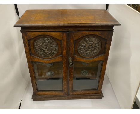 A VINTAGE OAK SMOKERS CABINET WITH CHERUB DESIGN CIRCULAR PLAQUES, INNER DRAWERS AND PULL OUT TRAY, 52 X 47 X 24CM 