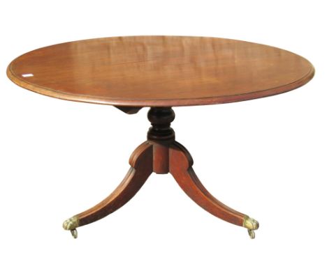 A Regency mahogany snap top dining table of circular form raised on a turned pillar and swept tripod with cast brass hairy pa