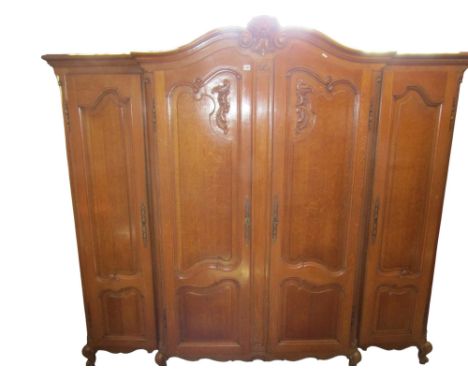 An oak shallow breakfront armoire enclosed by four fielded and moulded full length panelled doors within a panelled frame ben