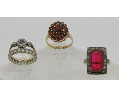 Four gem set rings comprising a 9ct daisy cluster ring set with blue and white sapphires, a 9ct garnet cluster ring, a 9ct wh