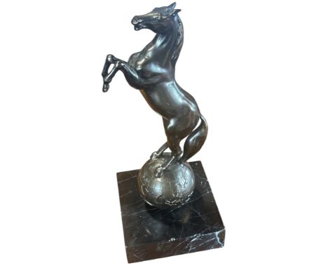 A bronze sculpture of a rearing horse on a globe raised on a marble plinth, 24cm high.