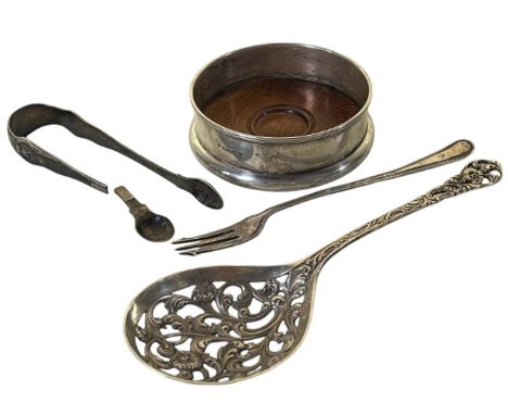 A silver wine coaster, a silver pickle fork, a broken sugar tong, and an elaborately scrolled silver plate serving spoon