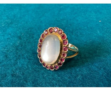 A moonstone and garnet ring, one oval cut white moonstone surrounded by 20 circular faceted cut garnets set in yellow metal, 