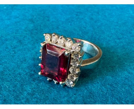 A tourmaline and diamond ring - one large red emerald cut tourmaline (12.00mm x 10.23mm x 6.8mm) surrounded by 18 round brill