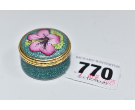A MOORCROFT ENAMEL PILL BOX, decorated with a floral design on a green ground and twist off lid, gilt detail around the edge 