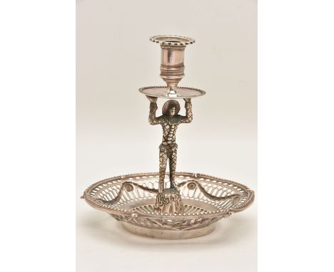 A WHITE METAL FIGURAL CANDLE STICK HOLDER, textured Harlequin figure holding up the drip pan and sconce, on a round pierced b