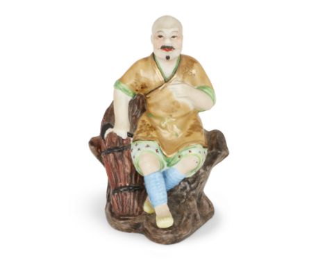 A Chinese famille rose seated figure of a workerMid-20th centurySeated on a rock by a wicker basket and holding a sickle, the
