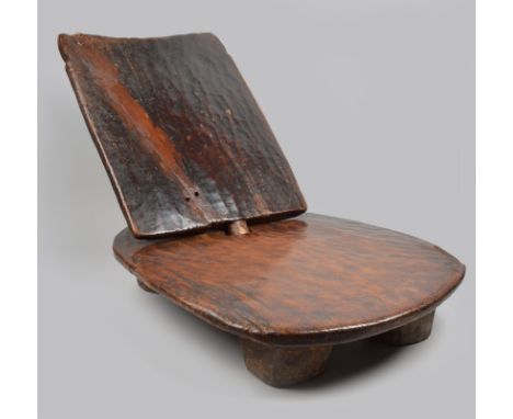 An Ethiopian low seat with an oblong seat raised on four short feet with a removable panel back, 60cm high. (2) Provenance Ma