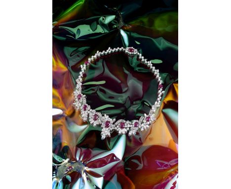 A RUBY AND DIAMOND NECKLACE, CIRCA 1960Set to the front with a graduated series of oval-cut rubies, within surrounds of brill