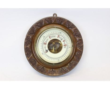Early 20th century aneroid barometer with enabled dial in a circular carved oak case, 23cm diameter