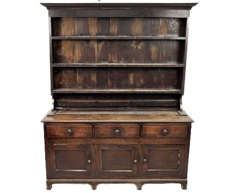 A George III oak dresser. The plate rack fitted three shelves, the base with three drawers above three panel doors, on bracke