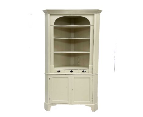 A late Victorian painted pine corner cupboard.  In two sections the upper with open shelves above twin cupboard doors on brac