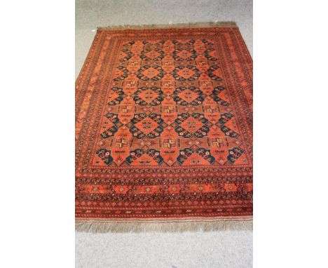 AN AFGHAN CARPET, 20th century, the field with repeating floral gul pattern in navy blue and red and brown within a multi gua