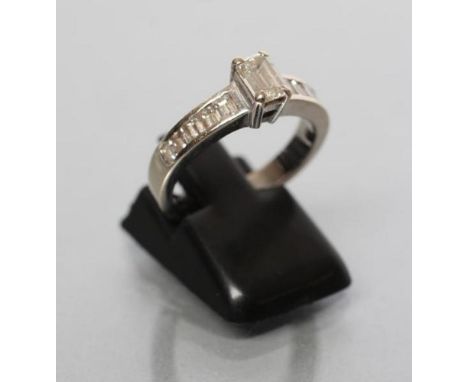 A DIAMOND RING, the baguette cut central stone of approximately 0.30cts claw set to shoulders each channel set with five slig