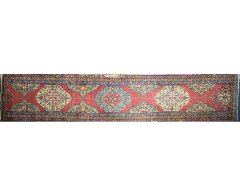 A 20th-century red ground Turkish carpet runner with four lozenges on a central pole within multiple borders. 416 cm x 83 cmC