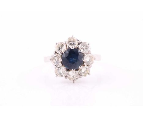 A sapphire and diamond cluster ring, the 6.8mm diameter dark blue sapphire within a surround of round brilliant cut diamonds,