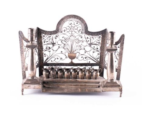 An antique white metal menorah, possibly Spanish, with urn and foliate design to the back, flanked by twill tall candlesticks